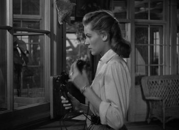 Movie still from “Key Largo” (1948), directed by John Huston – A woman holding a camera in front of an open window; Medium shot, Low angle