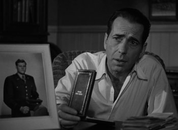 Movie still from “Key Largo” (1948), directed by John Huston – A black and white photo of a man holding a book; Close Up shot, Over the shoulder angle