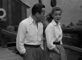 Movie still from “Key Largo” (1948), directed by John Huston – A man and a woman standing next to each other on a dock; Medium shot, Low angle