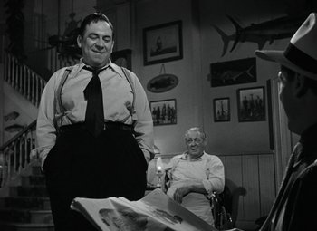 Movie still from “Key Largo” (1948), directed by John Huston – A man standing next to an older man in a room; Medium shot, Low angle
