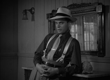 Movie still from “Key Largo” (1948), directed by John Huston – A man wearing a hat and suspenders in front of a mirror; Medium shot, Low angle