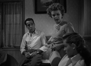 Movie still from “Key Largo” (1948), directed by John Huston – A man and a woman sitting next to each other in front of another woman; Medium shot, Over the shoulder angle