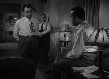 Movie still from “Key Largo” (1948), directed by John Huston – A group of men standing in a living room; Medium shot, Over the shoulder angle