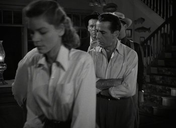 Movie still from “Key Largo” (1948), directed by John Huston – A group of people standing next to each other in a room; Medium shot, Over the shoulder angle