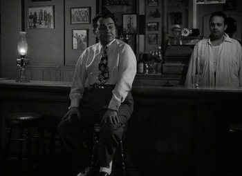 Movie still from “Key Largo” (1948), directed by John Huston – A black and white photo of a man sitting at a bar; Medium shot, Low angle