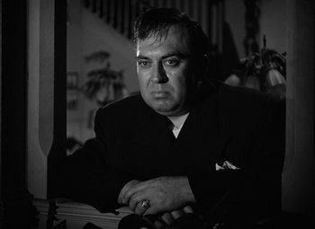 Movie still from “Key Largo” (1948), directed by John Huston – A black and white photo of a man sitting at a table; Close Up shot, Low angle
