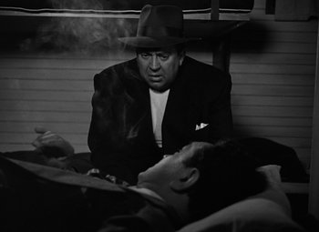 Movie still from “Key Largo” (1948), directed by John Huston – A man in a suit and a hat sitting next to a man in a bed; Medium shot, High angle