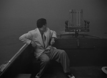 Movie still from “Key Largo” (1948), directed by John Huston – A black and white photo of a man sitting on a bench; Wide shot, High angle