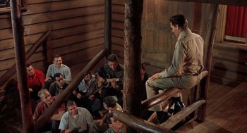 Movie still from “Kid Galahad” (1962), directed by Phil Karlson – A group of men sitting on a wooden railing; Wide shot, High angle