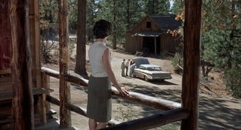 Movie still from “Kid Galahad” (1962), directed by Phil Karlson – A woman standing in front of a car in a wooded area; Wide shot, High angle