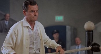 Movie still from “Kid Galahad” (1962), directed by Phil Karlson – A man in a white shirt and a white jacket holding onto a railing in front of a crowd; Medium shot, Low angle