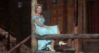Movie still from “Kid Galahad” (1962), directed by Phil Karlson – A woman in a blue dress sitting on a wooden railing; Medium shot, Low angle