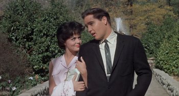 Movie still from “Kid Galahad” (1962), directed by Phil Karlson – A man and a woman standing next to each other in front of a fountain; Medium shot, Low angle
