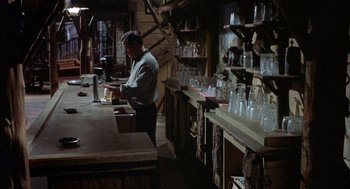 Movie still from “Kid Galahad” (1962), directed by Phil Karlson – A man standing at a counter in front of a bunch of glasses; Medium shot, High angle