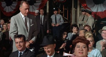 Movie still from “Kid Galahad” (1962), directed by Phil Karlson – A group of men and women sitting in a room together; Medium shot, Over the shoulder angle