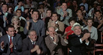 Movie still from “Kid Galahad” (1962), directed by Phil Karlson – A group of people sitting in a room clapping; Medium shot, High angle