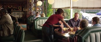 Movie still from “Kidnap” (2017), directed by Luis Prieto – A woman in a red shirt and a black apron at a table with food; Medium shot, Over the shoulder angle