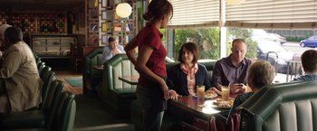 Movie still from “Kidnap” (2017), directed by Luis Prieto – A woman standing at a table in front of two other people; Medium shot, Over the shoulder angle