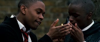Movie still from “Kidulthood” (2006), directed by Menhaj Huda – Two people are holding a candle in their hands; Close Up shot, Over the shoulder angle