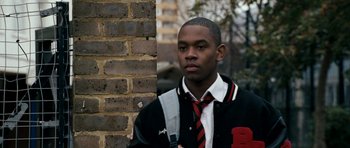 Movie still from “Kidulthood” (2006), directed by Menhaj Huda – A young man wearing a jacket and a tie standing in front of a brick wall; Close Up shot, Over the shoulder angle