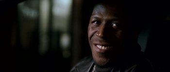 Movie still from “Kidulthood” (2006), directed by Menhaj Huda – A person wearing a leather jacket smiling; Close Up shot, Low angle