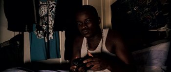 Movie still from “Kidulthood” (2006), directed by Menhaj Huda – A man sitting on a bed holding a remote control; Medium shot, High angle