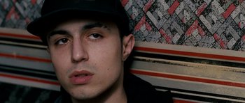 Movie still from “Kidulthood” (2006), directed by Menhaj Huda – A young man with a hat and a black shirt; Close Up shot, Overhead angle