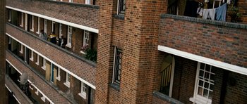 Movie still from “Kidulthood” (2006), directed by Menhaj Huda – A brick building has a balcony and a balcony railing; Extreme Wide shot, Overhead angle