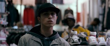 Movie still from “Kidulthood” (2006), directed by Menhaj Huda – A young man wearing a baseball cap and a jacket; Close Up shot, Low angle