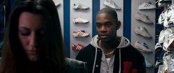 Movie still from “Kidulthood” (2006), directed by Menhaj Huda – A man in a black jacket is talking to a woman in front of a wall of shoes; Close Up shot, Over the shoulder angle