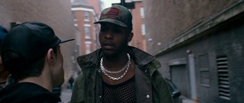 Movie still from “Kidulthood” (2006), directed by Menhaj Huda – A man wearing a baseball cap and a chain necklace; Close Up shot, Over the shoulder angle