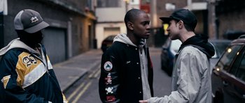 Movie still from “Kidulthood” (2006), directed by Menhaj Huda – Two young men talking on the side of the street; Medium shot, Over the shoulder angle