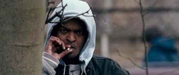 Movie still from “Kidulthood” (2006), directed by Menhaj Huda – A man smoking a cigarette while wearing a hoodie; Close Up shot, Low angle