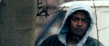 Movie still from “Kidulthood” (2006), directed by Menhaj Huda – A man in a hooded sweatshirt standing next to a tree; Close Up shot, Low angle