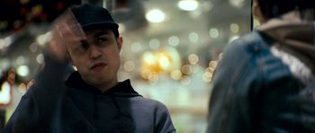 Movie still from “Kidulthood” (2006), directed by Menhaj Huda – A young man wearing a black hat and standing in front of blurry lights; Close Up shot, Over the shoulder angle