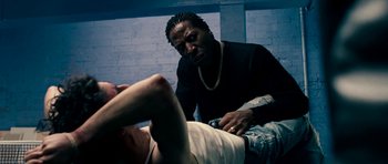 Movie still from “Kidulthood” (2006), directed by Menhaj Huda – A man is sitting on the ground with another man; Medium shot, Low angle