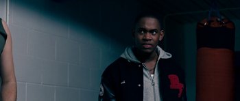 Movie still from “Kidulthood” (2006), directed by Menhaj Huda – A man in a black and gray jacket standing in a room; Close Up shot, Low angle