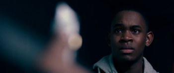 Movie still from “Kidulthood” (2006), directed by Menhaj Huda – A person holding a gun in a dark room; Close Up shot, Over the shoulder angle
