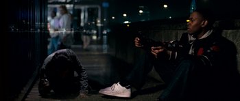 Movie still from “Kidulthood” (2006), directed by Menhaj Huda – A man sitting on the ground while holding a cell phone; Medium shot, High angle