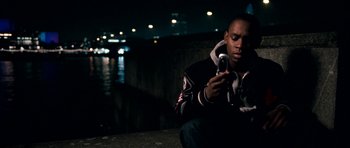 Movie still from “Kidulthood” (2006), directed by Menhaj Huda – A man sitting on the ground looking at his cell phone; Medium shot, High angle