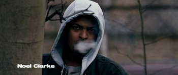 Movie still from “Kidulthood” (2006), directed by Menhaj Huda – A man with a hood is smoking a cigarette; Close Up shot, Low angle