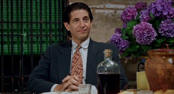 Movie still from “Kika” (1993), directed by Pedro Almodóvar – A man in a suit and tie sitting at a table; Medium shot, Over the shoulder angle