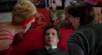 Movie still from “Kika” (1993), directed by Pedro Almodóvar – A man sitting on a red couch next to two other people; Medium shot, Over the shoulder angle