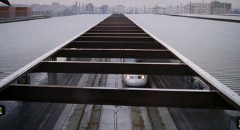 Movie still from “Kika” (1993), directed by Pedro Almodóvar – A train traveling down the tracks near a body of water; Extreme Wide shot, Low angle