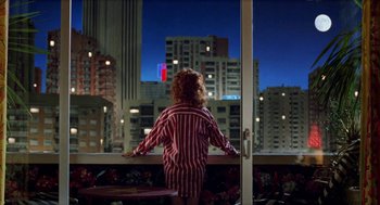 Movie still from “Kika” (1993), directed by Pedro Almodóvar – A woman standing in front of a window looking out at a city; Wide shot, Over the shoulder angle