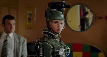 Movie still from “Kika” (1993), directed by Pedro Almodóvar – A woman in a green suit with a video camera on her head; Medium shot, Over the shoulder angle