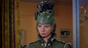 Movie still from “Kika” (1993), directed by Pedro Almodóvar – A woman wearing a green helmet with a video camera on top of it; Close Up shot, High angle