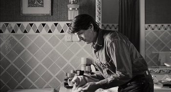 Movie still from “Kika” (1993), directed by Pedro Almodóvar – A black and white photo of a man in a kitchen; Medium shot, Over the shoulder angle