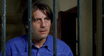 Movie still from “Kika” (1993), directed by Pedro Almodóvar – A man in a blue shirt behind a metal fence; Close Up shot, Low angle