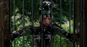 Movie still from “Kika” (1993), directed by Pedro Almodóvar – A woman in military gear behind a metal fence; Medium shot, High angle